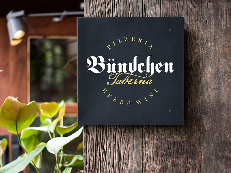 Placa com o logotipo da Bündchen Pizzaria em um ambiente rústico.